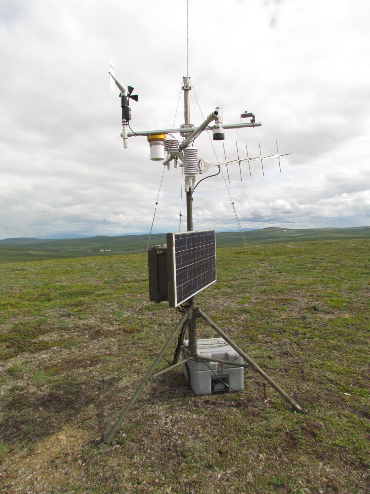 Remote monitoring station on a tripod with a solar panel and radio antenna on open grassland